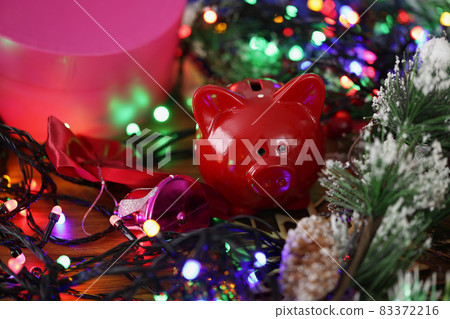 Red piggy bank standing among bright shiny new year garland closeup Red piggy bank standing among bright shiny new year garland closeup 83372216