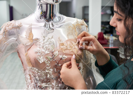 Dressmaker fixing white lace wedding dress on a mannequin in tailor studio Dressmaker fixing white lace wedding dress on a mannequin in tailor studio 83372217