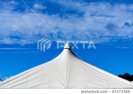 A tent with a white pointed roof against the backdrop of a cloud-printed autumn sky A tent with a white pointed roof against the backdrop of a cloud-printed autumn sky 83373369