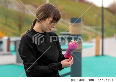 young woman wrapping a wrist wrap around her hand before outdoor martial arts training young woman wrapping a wrist wrap around her hand before outdoor martial arts training 83373503