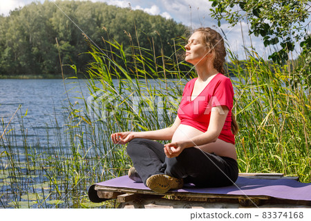 Pregnant woman doing yoga exercise meditating in a summer forest Pregnant woman doing yoga exercise meditating in a summer forest 83374168