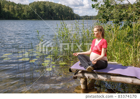 Pregnant woman doing yoga exercise meditating in a summer forest Pregnant woman doing yoga exercise meditating in a summer forest 83374170