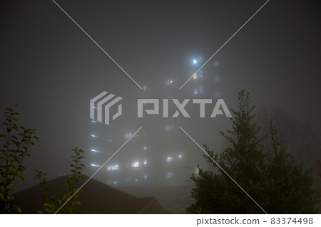 Eerie sky scraper hospital lights shine through very thick fog. 83374498