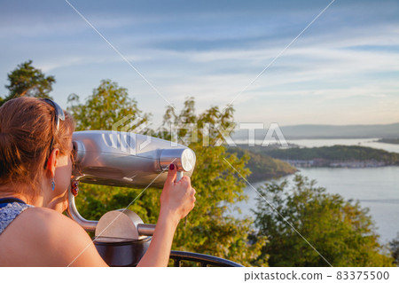 Tourist observing Oslofjord through tourist telescope at sunset Oslo Norway 83375500
