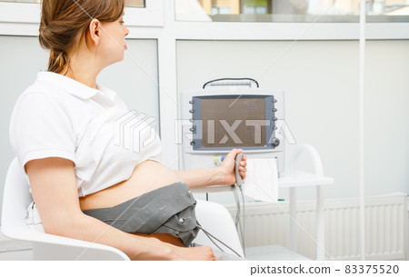 Pregnant woman performing cardiotocography CTG monitoring fetal heartbeat 83375520