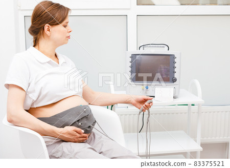 Pregnant woman performing cardiotocography CTG monitoring fetal heartbeat 83375521