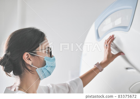 woman radiologist doctor adjusting computer tomography scanner machine to make CT test. female technician with face mask on working in a hospital or clinic for covid-19 patients.  83375672