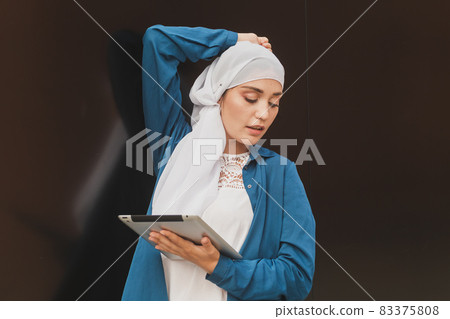 Portrait of an Arab student girl holding a tablet. Arab business woman in hijab holding a tablet in the street. Woman is dressed in hijab 83375808