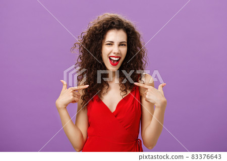 Woman celebrating successful sign of deal, pleased and satisfied bragging about own achievements pointing at herself smiling joyfully with triumph standing in evening red dress over purple background Woman celebrating successful sign of deal, pleased and satisfied bragging about own achievements pointing at herself smiling joyfully with triumph standing in evening red dress over purple background 83376643