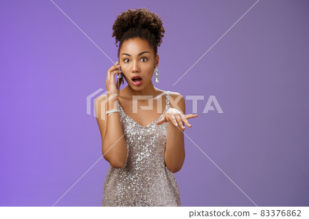 Astonished shocked african american woman gossiping talking smartphone drop jaw astonished holding phone ear raise hand dismay concerned standing speechless hear rumour, standing blue background Astonished shocked african american woman gossiping talking smartphone drop jaw astonished holding phone ear raise hand dismay concerned standing speechless hear rumour, standing blue background 83376862