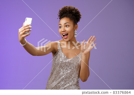Friendly stylish confident african-american woman in silver glittering dress waving raised palm hello hi gesture record video smartphone greeting internet followers blogging during party Friendly stylish confident african-american woman in silver glittering dress waving raised palm hello hi gesture record video smartphone greeting internet followers blogging during party 83376864