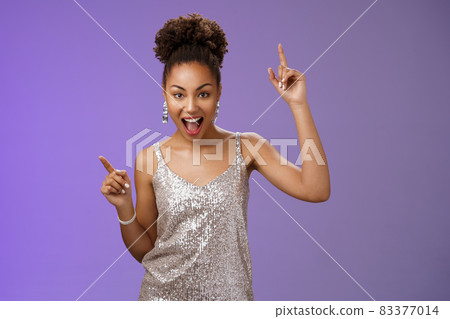 Sassy good-looking african-american woman in trendy glamour silver shiny dress index fingers raised up smiling cheeky joyfully celebrating great lucky news dancing grinning, standing blue background Sassy good-looking african-american woman in trendy glamour silver shiny dress index fingers raised up smiling cheeky joyfully celebrating great lucky news dancing grinning, standing blue background 83377014