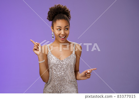 Good-looking excited glamour african-american female student attend luxurious event in silver shiny perfect dress dancing look around pointing right left smiling pleased variants make choice 83377015