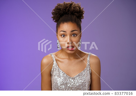 Awkward cute african-american woman in silver glamour dress clench teeth look worried complicated say oops make mistake accidently spill drink standing unsure insecure blue background Awkward cute african-american woman in silver glamour dress clench teeth look worried complicated say oops make mistake accidently spill drink standing unsure insecure blue background 83377016