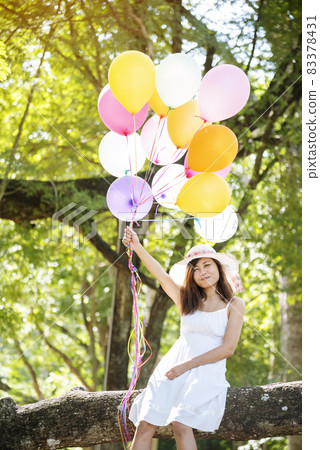 Cheerful beauty woman holding balloons relax sitting under big tree in green park with happiness. Woman Hands holding vibrant air balloons play on birthday party happy time summer on sunshine outdoor Cheerful beauty woman holding balloons relax sitting under big tree in green park with happiness. Woman Hands holding vibrant air balloons play on birthday party happy time summer on sunshine outdoor 83378431