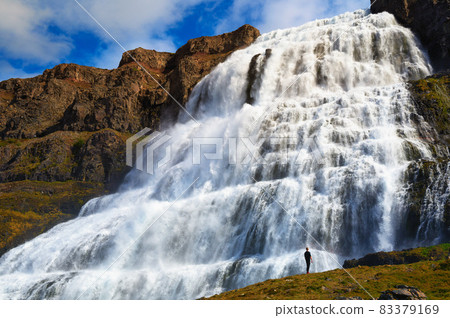 Person standing at the Dynjandi waterfall on the Westfjords peninsula in Iceland Person standing at the Dynjandi waterfall on the Westfjords peninsula in Iceland 83379169