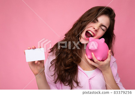 Attractive happy emotional young brunette woman wearing shirt isolated on pink background with empty 83379256
