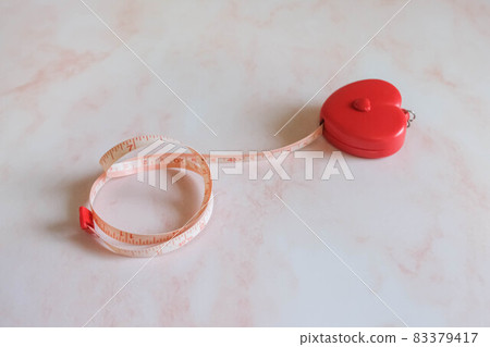 Tape measure in the heart shape on the pink marble background. 83379417