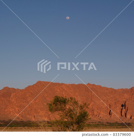 solitary moon at dusk, orange mountains and blue sky. desert landscape 83379600
