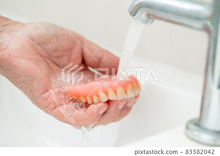 Asian senior or elderly old woman patient holding and washing denture in nursing hospital ward; healthy strong medical concept 83382042