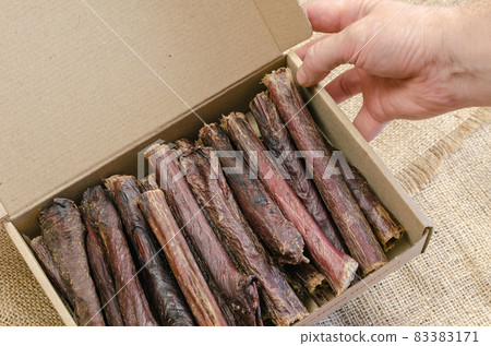 Hand holds cardboard box of dog treats. Sticks of dried beef eso 83383171