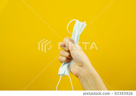A hand holding a medical protective mask on a yellow background. Virus protection. An epidemic A hand holding a medical protective mask on a yellow background. Virus protection. An epidemic 83383926