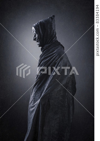 Spooky figure with hooded cape over dark misty background 83384194