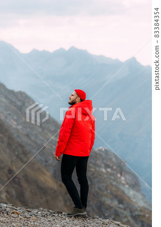 A man stands with his back in the mountains. Traveler in the mountains, vertical view. A man enjoys a beautiful view of the mountains. Man on the background of mountains. Copy space 83384354