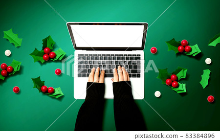 Person using a laptop computer with Christmas holly berries Person using a laptop computer with Christmas holly berries 83384896