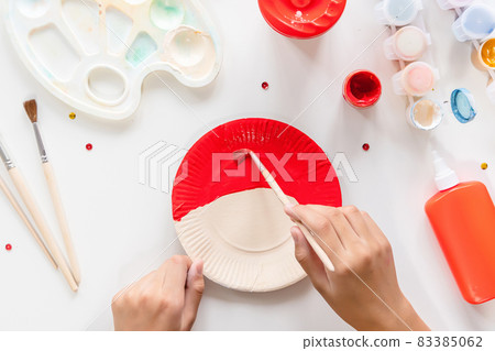 The child glues the parts Santa made from paper plate. Handmade. Project of children's creativity, handicrafts, crafts for kids. Preparation for christmas. Decoration. 83385062