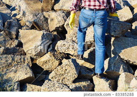 a man works with a pile of stones and broken pieces of concrete, carries construction debris a man works with a pile of stones and broken pieces of concrete, carries construction debris 83385288