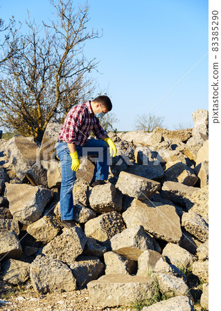 a man works with a pile of stones and broken pieces of concrete, carries construction debris a man works with a pile of stones and broken pieces of concrete, carries construction debris 83385290