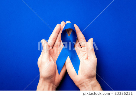 Blue ribbon cancer. Awareness prostate cancer of men health in November. Blue ribbon in hands isolated on deep blue background. Symbol of oncology affected man. Copy space. Blue ribbon cancer. Awareness prostate cancer of men health in November. Blue ribbon in hands isolated on deep blue background. Symbol of oncology affected man. Copy space. 83386231