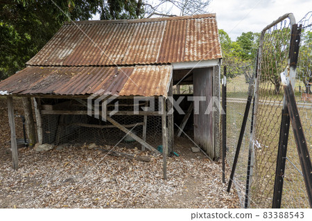 An old dilapidated rusting chicken house fenced with netted wire, empty and no longer in use 83388543