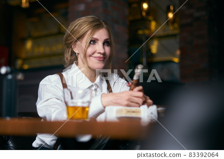 beautiful senior woman on an armchair in hat smoking cigare 83392064