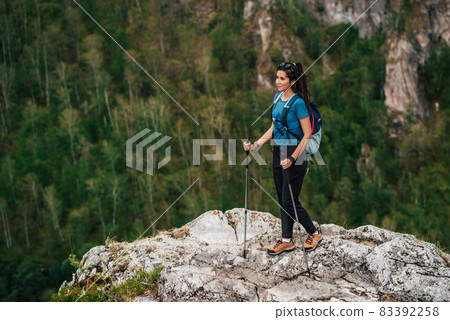 Hiking in the mountains. The concept of active recreation. Traveling woman with a backpack on the background of mountains. Female traveler with a backpack hiking in the mountains. Copy space Hiking in the mountains. The concept of active recreation. Traveling woman with a backpack on the background of mountains. Female traveler with a backpack hiking in the mountains. Copy space 83392258