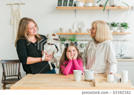 Happy granddaughter and grandmother and daughter having fun with jack russell terrier dog. Grandma hugs grandchild at home. Relationship, family and three generation concept. Happy granddaughter and grandmother and daughter having fun with jack russell terrier dog. Grandma hugs grandchild at home. Relationship, family and three generation concept. 83392582