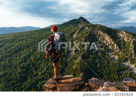 A traveler with a backpack in the mountains at sunset. Hiking in the mountains. Travel to Bashkiria, Russia. A man with a backpack on the background of the mountains, a rear view. Backpacking trips A traveler with a backpack in the mountains at sunset. Hiking in the mountains. Travel to Bashkiria, Russia. A man with a backpack on the background of the mountains, a rear view. Backpacking trips 83392928