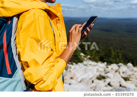 A traveler with a phone, close-up.Young woman wearing yellow windbreaker use smartphone search map at countryside background. Adult woman holding and using smartphone. Travel and active lifestyle A traveler with a phone, close-up.Young woman wearing yellow windbreaker use smartphone search map at countryside background. Adult woman holding and using smartphone. Travel and active lifestyle 83395070