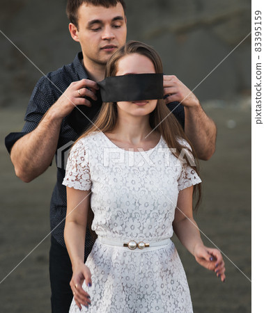 Romantic man blindfolding his woman with black ribbon. Love blind concept 83395159