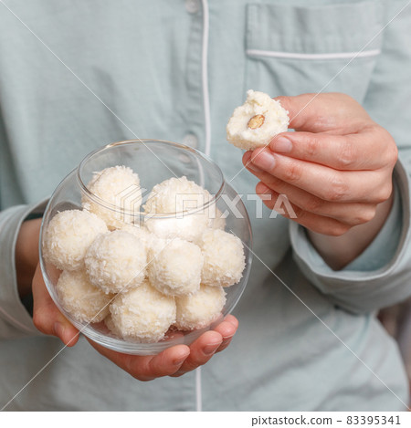 Coconut candy balls in glass bowl in hands of woman 83395341
