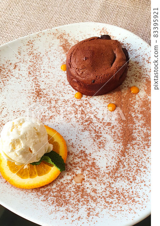 Close up of hot melting chocolate cake dessert and scoop of vanilla ice cream on orange slice on white plate. Chocolate fondant and ice cream. Top view, vertical photo. 83395921