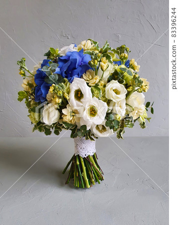 Round bridal wedding bouquet on gray concrete background. The wedding bouquet consists of freesia, Matthiola, lisianthus, dianthus, blue Hydrangea and green eucalyptus. Front view, closeup. 83396244