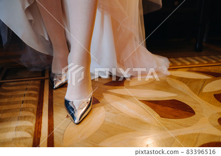 Close-up of women's shoes and the hem of a wedding dress. The bride's foot in a silver slipper Close-up of women's shoes and the hem of a wedding dress. The bride's foot in a silver slipper 83396516