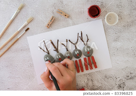 Merry Christmas deer on greeting card postcard made of pebbles, sea stones, clothespins and branches on white background. Diy Natural Eco style diy. Gift idea. Step by step. Top view. 83396825