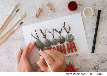 Diy Merry Christmas deer on greeting card postcard made of pebbles, sea stones, clothespins and branches on white background. Natural Eco style diy. Gift idea. Step by step. Top view. Diy Merry Christmas deer on greeting card postcard made of pebbles, sea stones, clothespins and branches on white background. Natural Eco style diy. Gift idea. Step by step. Top view. 83396826