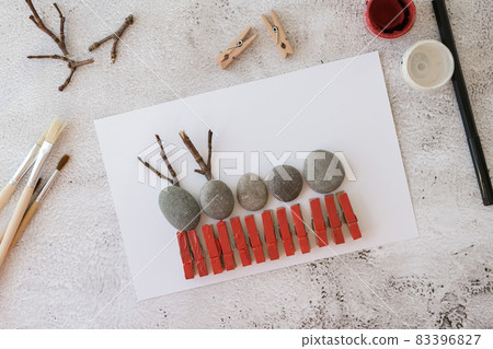 Merry Christmas deer on greeting card postcard made of pebbles, sea stones, clothespins and branches on white background. Diy Natural Eco style diy. Gift idea. Step by step. Top view. Merry Christmas deer on greeting card postcard made of pebbles, sea stones, clothespins and branches on white background. Diy Natural Eco style diy. Gift idea. Step by step. Top view. 83396827