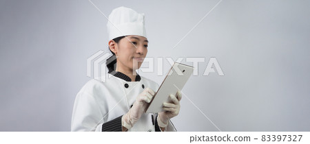 Asian woman chef holding smartphone or digital tablet and received order from online shop or merchant application. she smiling in chef uniform and standing in white background. Online food merchant. Asian woman chef holding smartphone or digital tablet and received order from online shop or merchant application. she smiling in chef uniform and standing in white background. Online food merchant. 83397327