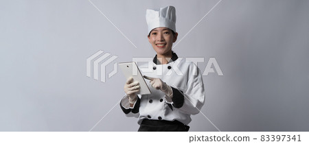 Asian woman chef holding smartphone or digital tablet and received order from online shop or merchant application. she smiling in chef uniform and standing in white background. Online food merchant. Asian woman chef holding smartphone or digital tablet and received order from online shop or merchant application. she smiling in chef uniform and standing in white background. Online food merchant. 83397341