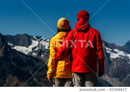 People in colorful jackets on the background of the mountains, rear view. An active couple is engaged in Hiking. A young couple is engaged in tracking. Hiking. People in the mountains People in colorful jackets on the background of the mountains, rear view. An active couple is engaged in Hiking. A young couple is engaged in tracking. Hiking. People in the mountains 83398617